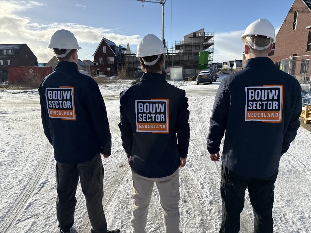 Drie vakmensen van Bouwsector Nederland met witte helm en bedrijfsjas op een nieuwbouwplaats